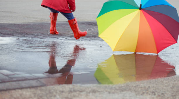 istock Jumping child with color umbrella in muddy puddle. 658587940