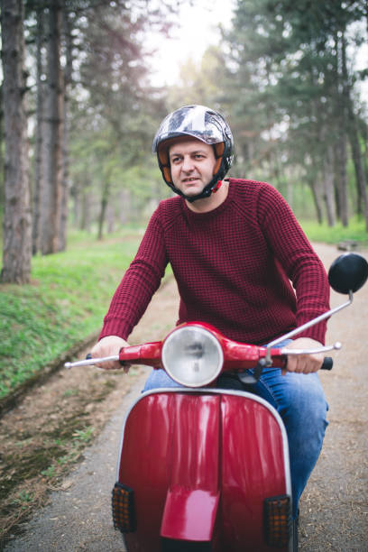 Young hipster man in helmet sitting on a vintage scooter .