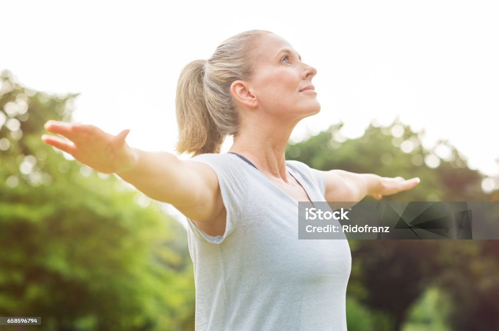 Mature woman yoga exercise Mature woman doing yoga at park and looking away. Senior blonde woman enjoying nature during a breathing exercise. Portrait of a fitness woman stretching arms and looking away outdoor. "r Women Stock Photo