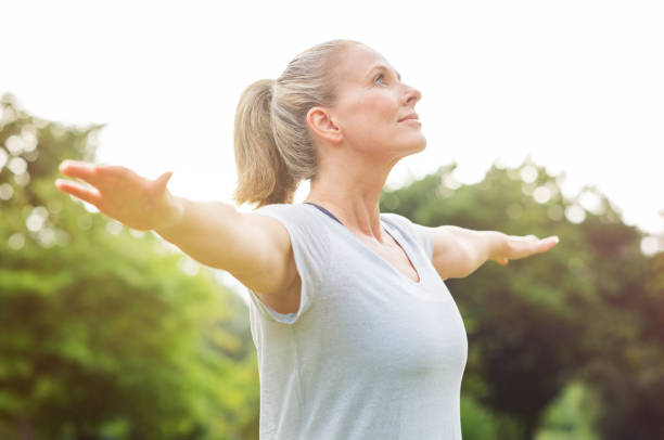 Mature woman yoga exercise Mature woman doing yoga at park and looking away. Senior blonde woman enjoying nature during a breathing exercise. Portrait of a fitness woman stretching arms and looking away outdoor. "r mid adult stock pictures, royalty-free photos & images