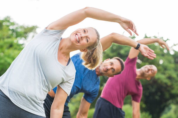 People doing stretching exercise Group of mature healthy people doing stretching at park. Fitness middle aged group exercising outdoor. Three happy people in a row doing stretching arm and smiling. mid adult women stock pictures, royalty-free photos & images