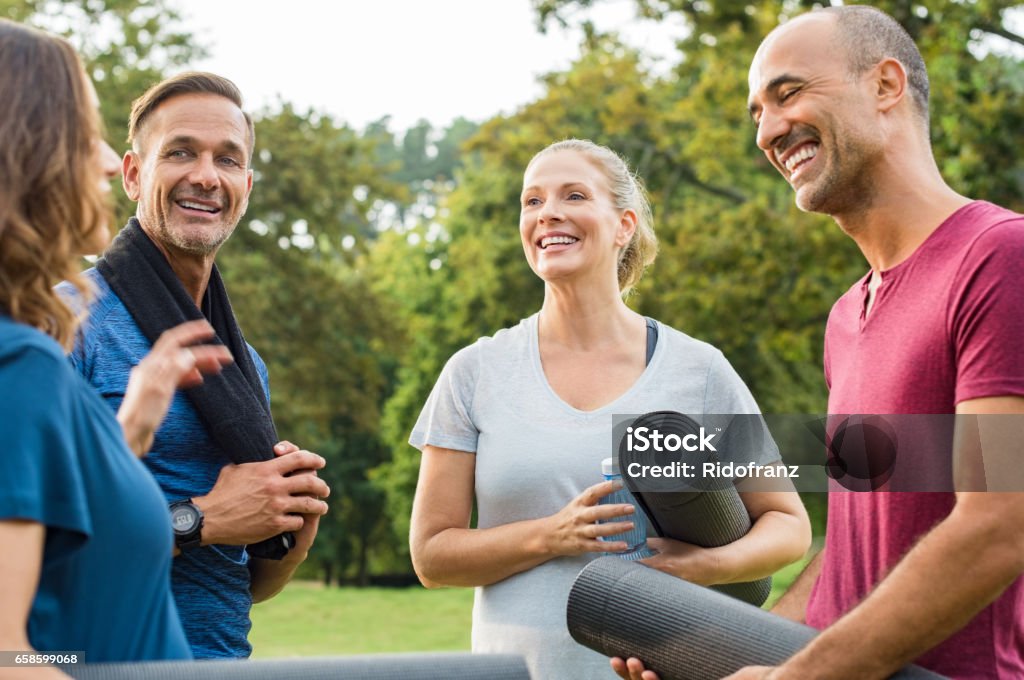 Mature fitness friends talking Happy multiethnic group of mature people holding yoga mat and towel in conversation after exercising at park. Happy senior men and smiling women talking to each other after an exercising class outdoor. "r Outdoors Stock Photo