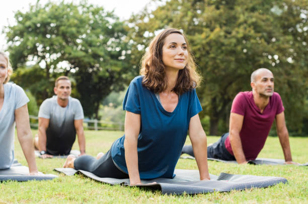 Class doing yoga Mature healthy people doing yoga at park. Group of multiethnic people exercising on green grass with yoga mat. Happy men and smiling women in yoga class doing exercise outdoor."r mid adult men stock pictures, royalty-free photos & images