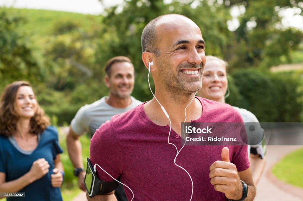 Happy people running Portrait of a happy cheerful man listening to music while jogging. Man listening to music while jogging with group. Happy trainer in park running with team."r Exercising Stock Photo