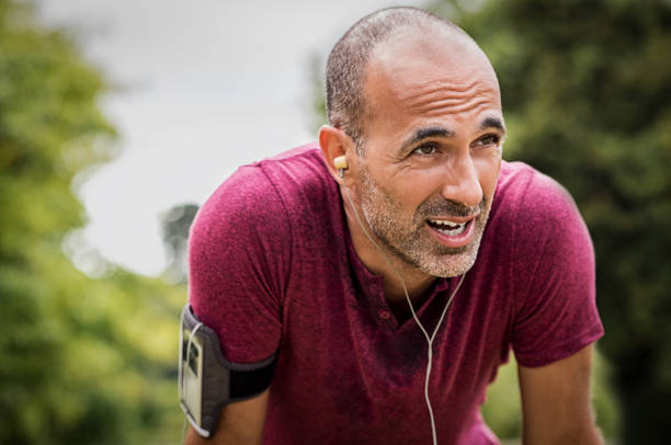 Sweaty mature jogger Portrait of athletic mature man after run. Handsome senior man resting after jog at the park on a sunny day. Sweaty multiethnic man listening to music while jogging. exhaustion photos stock pictures, royalty-free photos & images