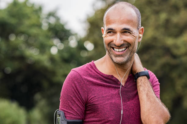 Sweaty man resting after exercise Mature man listening to music while resting after jogging. Happy bald senior man feeling refreshed after exercise. Portrait of a multiethnic man looking away in park while listening to music after fitness. running motion stock pictures, royalty-free photos & images