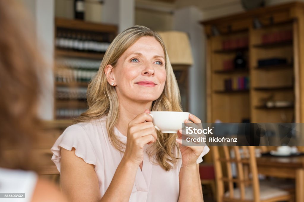 Woman thinking over coffee Mature woman holding coffee cup and looking away at cafeteria. Thoughtful mature woman thinking while holding coffee cup. Happy and satisfied woman enjoying cappuccino at cafe. Women Stock Photo