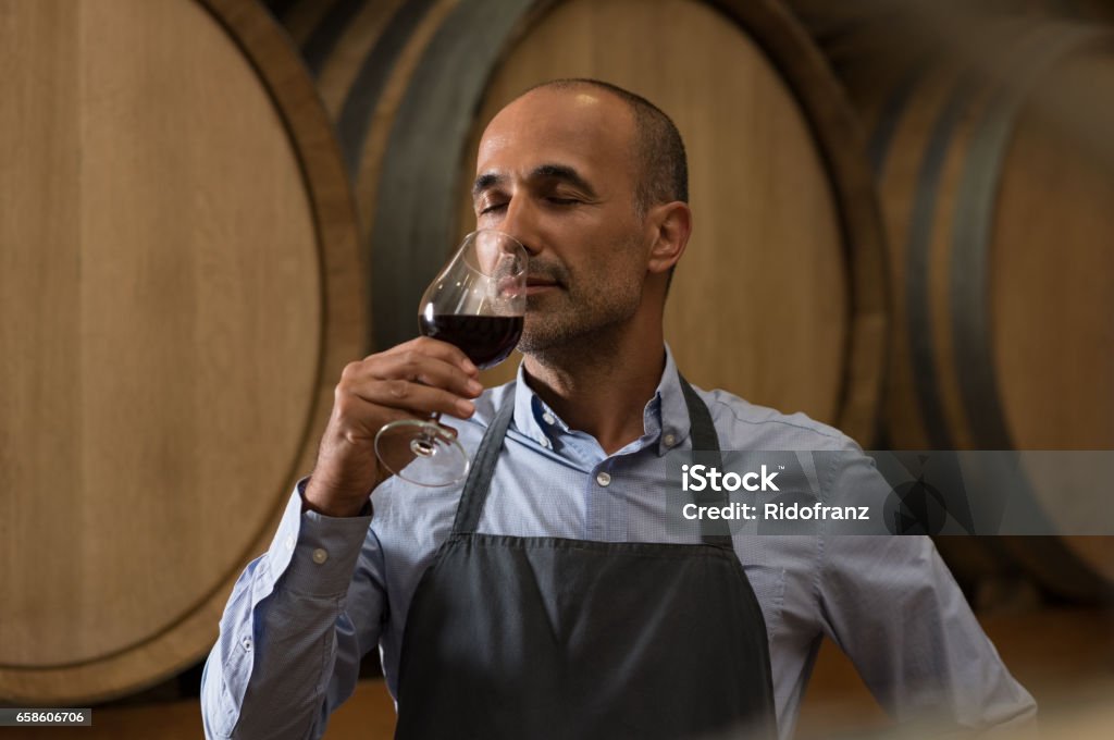 Winemaker tasting wine Winemaker smelling a glass of red wine in a traditional cellar surrounded by wooden barrels. Professional mature man smelling red wine in glass with closed eyes in a wine cellar. Sommelier inspecting wine."r Wine Stock Photo