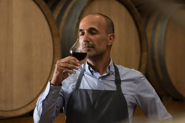 Winemaker tasting wine Winemaker smelling a glass of red wine in a traditional cellar surrounded by wooden barrels. Professional mature man smelling red wine in glass with closed eyes in a wine cellar. Sommelier inspecting wine."r sommelier photos stock pictures, royalty-free photos & images