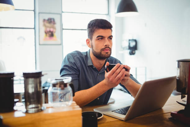 istock Thoughtful man having cup of coffee with laptop on table 658609756