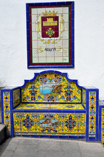 FIRGAS, SPAIN - FEB 26, 2014:  Fragment of an architectural monument in Firgas, bench from Andalusian tiles depicting the city Agaete. One from main attraction in this city