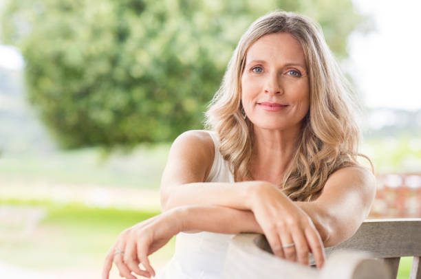 Senior woman relaxing Happy senior woman relaxing on bench in the lawn. Close up face of a mature blonde woman smiling and looking at camera. Retired woman in casuals sitting outdoor in a summer day. smirking stock pictures, royalty-free photos & images