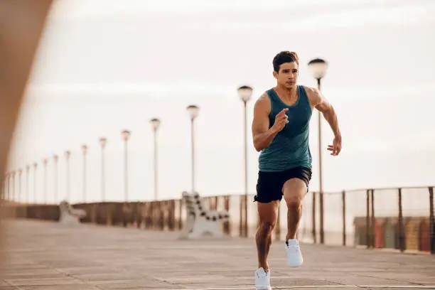Full length shot of healthy young man running on the promenade. Male runner sprinting outdoors.