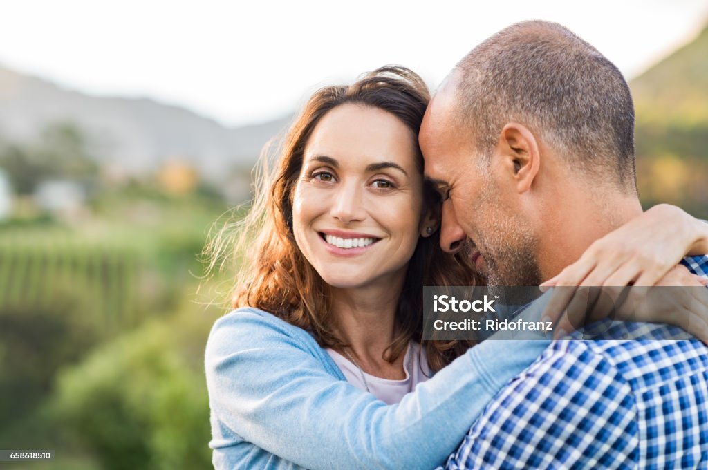 Mature romantic couple Mature romantic couple embracing outdoor. Happy woman embracing her multiethnic boyfriend at park during sunset. Smiling brunette woman in love with her husband looking at camera. Couple - Relationship Stock Photo