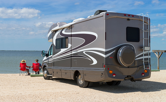 Senior ouple sitting near water with motorhome in camping