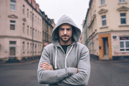 Close-up portrait of a stylish young man standing in a city street. Young male looking at camera and wearing hoodie.