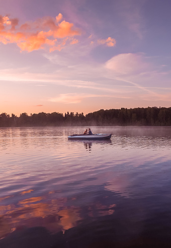 A beautiful golden sunset on the river. Lovers ride in a boat on a lake during a beautiful sunset. Happy couple woman and man together relaxing on the water. The beautiful nature around. Russia Ruza Reservoir
