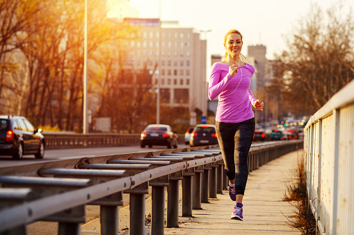 Young beautiful woman running on the sidewalk besides traffic road in the city