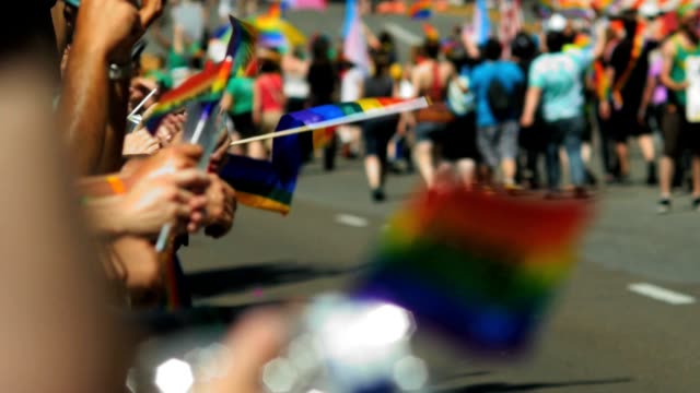 People clap, cheer and hold wave rainbow flags as gay pride parade marchers walk