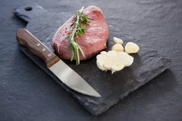 Sirloin chop, knife and garlic on slate plate against black background