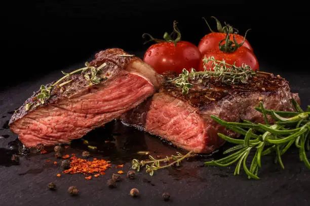 Sliced grilled beef steak with spices on slate slab on dark background