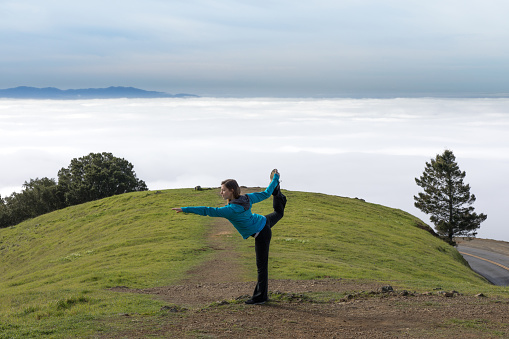 Warrior yoga posture of young woman above the clouds. Mount Tamalpais, California, USA