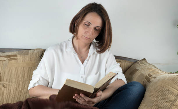 istock Young woman reading a book on a couch 658688598