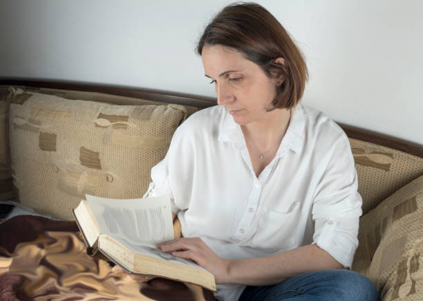 istock Young woman reading a book on a couch 658688642