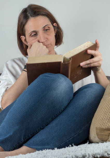 istock Young woman reading a book on a couch 658688978