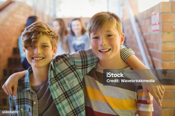 Portrait Of Smiling Schoolboys Standing With Arm Around In Corridor Stock Photo - Download Image Now