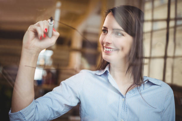 istock Businesswoman smiling while writing on glass with marker pen 658713548