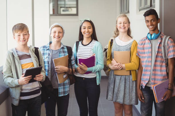 istock Portrait of smiling students standing with notebook and school bag in corridor 658744372