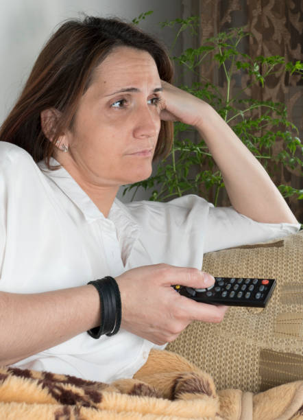 Young woman watching TV with remote in hands stock photo