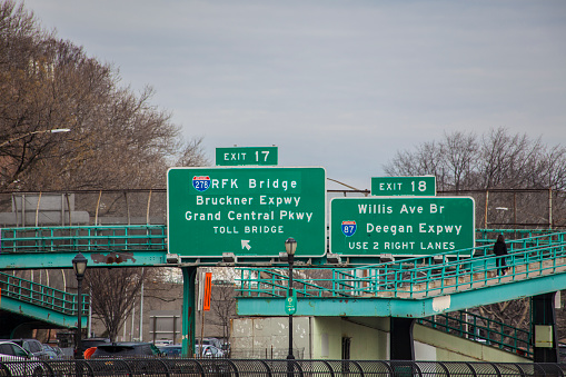 An editorial stock photo of the RFK Bridge or Robert F. Kennedy Bridge road sign in New York City, USA. A person can be seen walking onto the bridge above the busy traffic below.