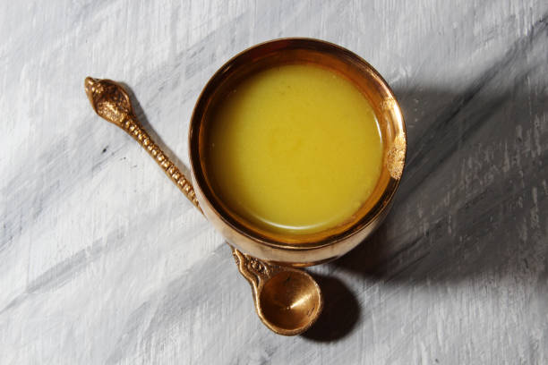 Ghee or clarified butter Ghee or clarified butter in a copper container with a spoon on a wooden gray background.Top view. clarified butter stock pictures, royalty-free photos & images