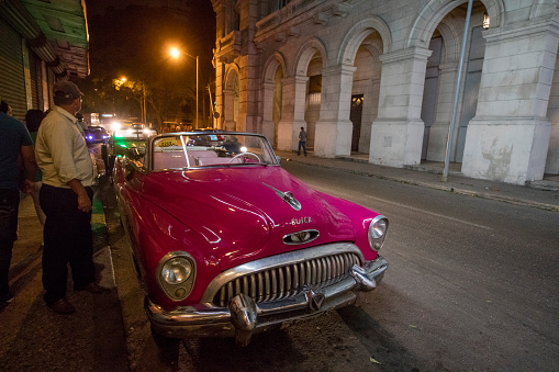 Buick antique car on the street. Incidental people on the background.