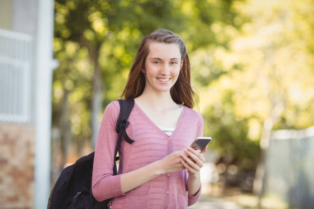 istock Smiling school girl with schoolbag using mobile phone in campus 658836026