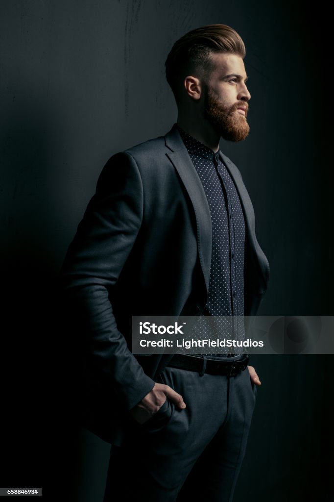 Stylish handsome bearded man in trendy suit looking away on black Men Stock Photo