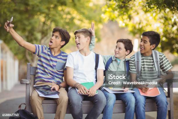 Happy Students Sitting On Bench And Taking Selfie On Mobile Phone Stock Photo - Download Image Now