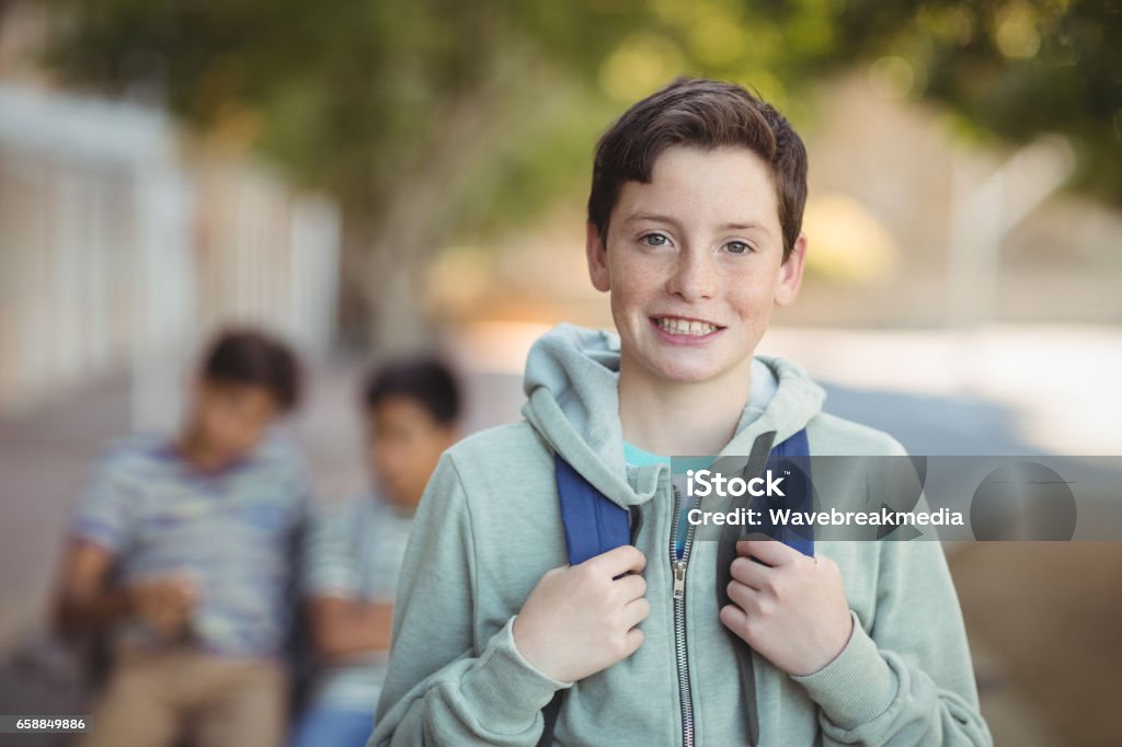 Smiling schoolboy standing with schoolbag in campus Portrait of smiling schoolboy standing with schoolbag in campus Teenage Boys Stock Photo