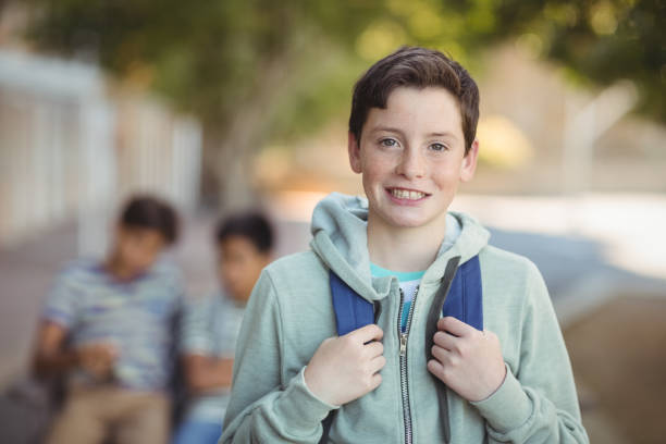 улыбающийся школьник, стоящий со школьной сумкой в кампусе - 14 стоковые фото и изображения