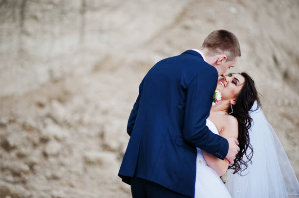 istock Young stylish wedding couple against sandy career at cloudy sky. 658890380
