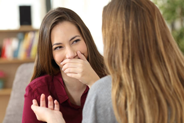 Ashamed woman hiding her smile in a conversation Ashamed woman hiding her smile in a conversation with a friend sitting on a couch at home tooth in hand stock pictures, royalty-free photos & images