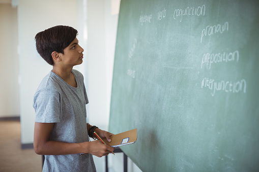 Attentive schoolboy reading chalkboard in classroom at school