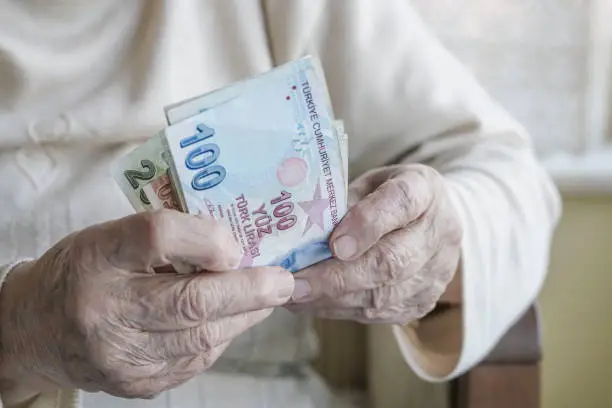 Photo of Closeup of wrinkled hands holding turkish lira banknotes