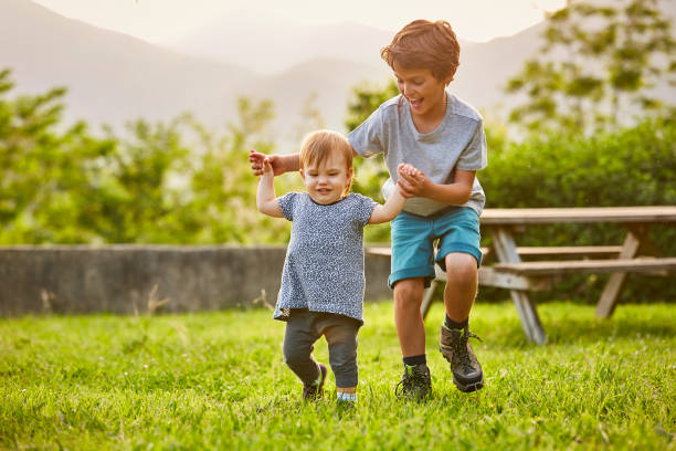 happy boy playing with toddler on grassy field - babies or child foto e immagini stock