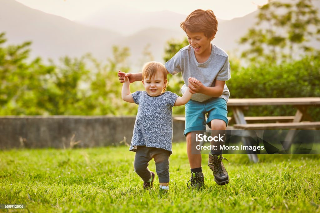 Happy boy playing with toddler on grassy field Happy boy playing with toddler on grassy field. Kids are wearing casuals. They are enjoying at back yard. Child Stock Photo