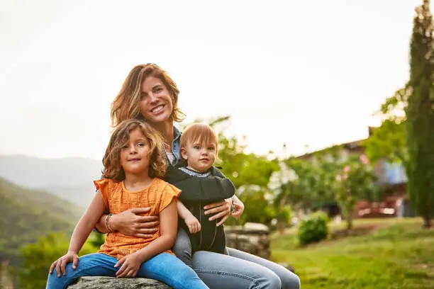Photo of Portrait of smiling mother carrying kids at yard