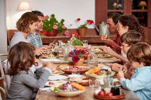 Parents and children having food at dining table. Friends and families sitting together at home. They are in casuals.