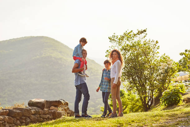 Full length of family standing on grassy field Full length of family standing on grassy field. Parents and children are spending leisure time on sunny day. They are against mountain. mid distance stock pictures, royalty-free photos & images